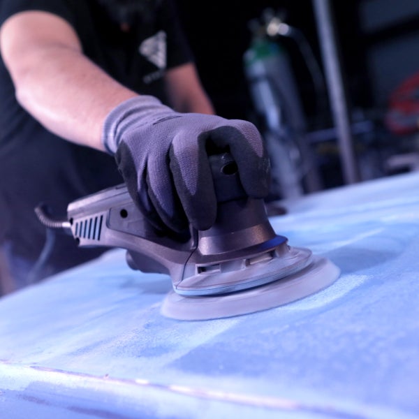 Eine Person schleift eine Oberfläche mit einem Exzenterschleifer.