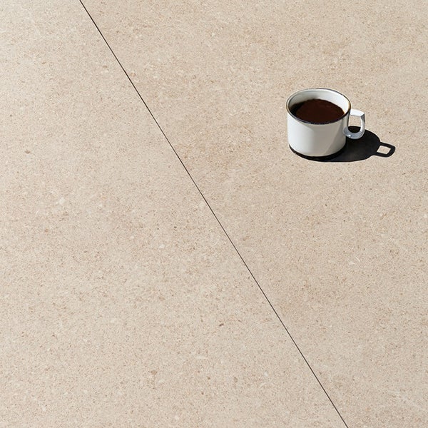 Steinzeugfliese mit sandartiger Oberflächenstruktur und Kaffeetasse auf der Oberfläche.