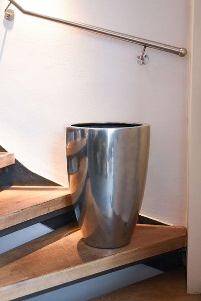Konischer Pflanzkübel aus Metall auf einer Holztreppe neben einem Handlauf.