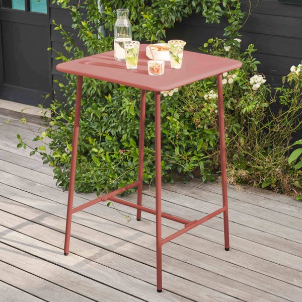 Quadratischer Stehtisch aus Metall auf einer Holzterrasse im Garten, dekoriert mit Gläsern und einer Karaffe auf der Tischplatte.