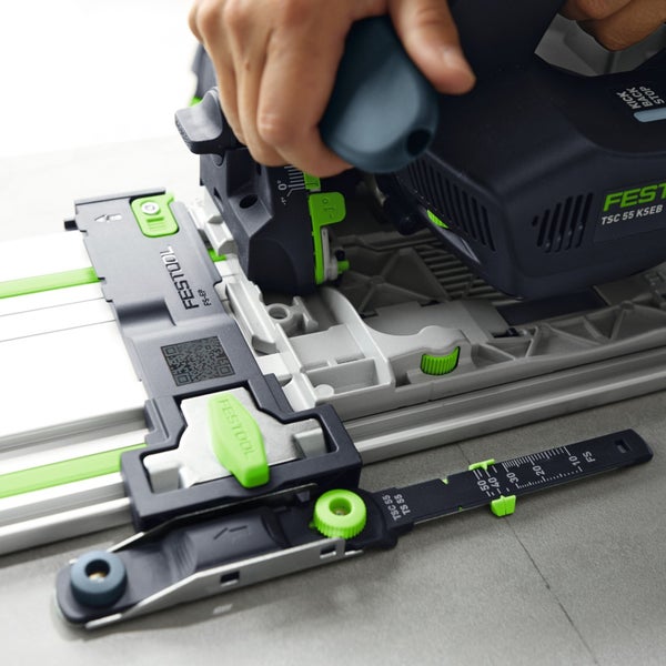 Festool Tauchkreissäge auf einer Führungsschiene mit montiertem Zubehör und Skala, geführt von einer Hand.