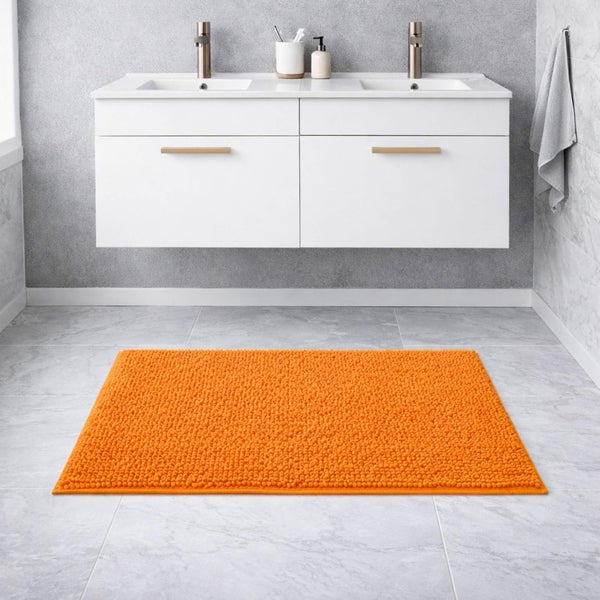 Modernes Badezimmer mit einem orangefarbenen Badeteppich auf hellen Bodenfliesen vor einem weißen Doppelwaschtisch mit zwei Armaturen.