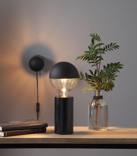 Dekorative Tischleuchte mit Leuchtmittel und Vase mit Zweigen auf einem Tisch