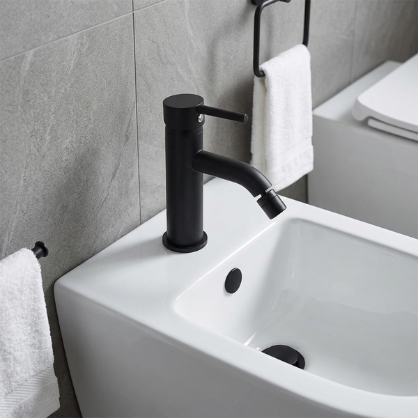 Schwarze Einhebel-Bidetarmatur aus Metall auf einem weißen Keramik-Bidet in einem hellen, modernen Badezimmer.
