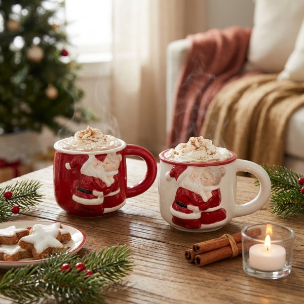 Zwei Weihnachtstassen mit Santa Claus Motiv gefüllt mit heißem Kakao auf einem Holztisch mit Weihnachtsdekoration.