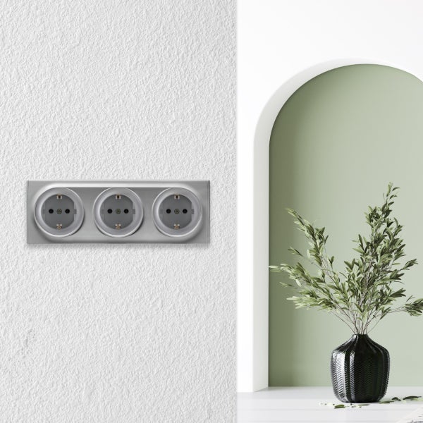 Dreifach Steckdose auf einer strukturierten Wand mit einem Torbogen im Hintergrund und einer Pflanze in einer Vase.