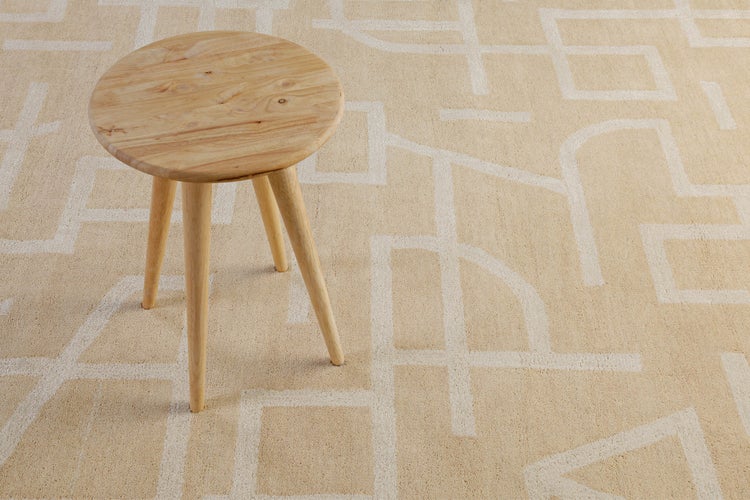 Moderner Teppich mit geometrischem Muster und ein runder dreibeiniger Hocker aus Holz.