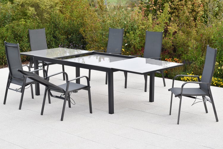 Modernes Gartenmöbel-Set bestehend aus einem rechteckigen Tisch mit Glasplatte und sechs passenden Stühlen auf einer Steinterrasse im Garten.