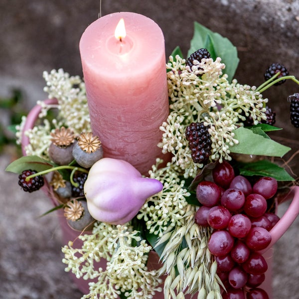Dekorative Anordnung mit Kerze, Beeren, Weintrauben und Zierfrüchten in einem Behälter