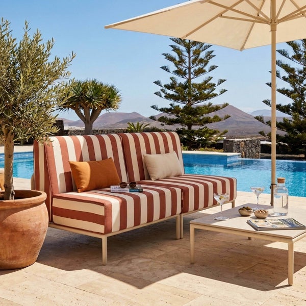 Gestreiftes Zweisitzer-Gartensofa mit Kissen, flachem Loungetisch und Sonnenschirm auf einer Steinterrasse am Pool.