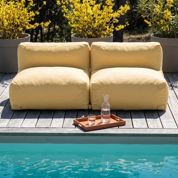 Zwei Outdoor-Lounge-Sitzsäcke in einer hellen Szene auf einer Holzterrasse am Pool mit Tablett, Karaffe und Pflanzen im Hintergrund.