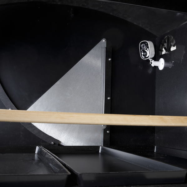 Innenansicht eines Hühnerstalls mit installierter Überwachungskamera, hölzerner Sitzstange und schwarzen Reinigungswannen.