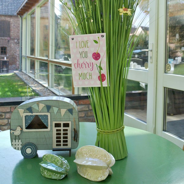 Dekoratives Arrangement mit Wohnwagen, Dekoschild, Kunstpflanze und Keramikfiguren auf einem Tisch