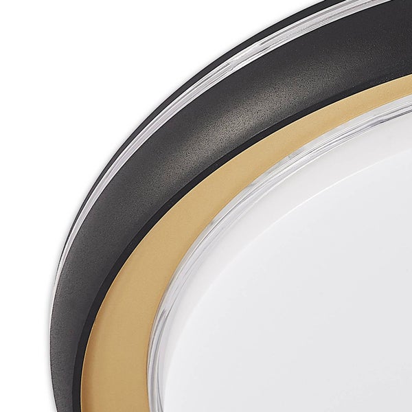 Detailansicht einer runden Leuchte mit konzentrischen Ringen aus schwarzem Kunststoff mit Struktur, goldfarbenem Metall und weißem Kunststoff.