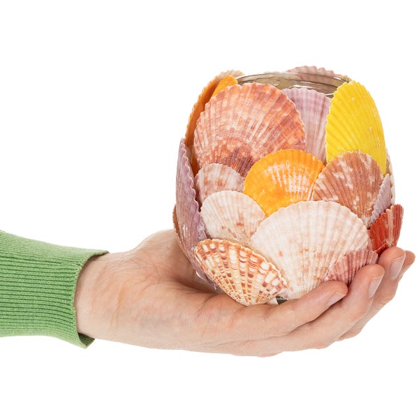 Hand hält ein mit bunten Muscheln dekoriertes Glasgefäß.