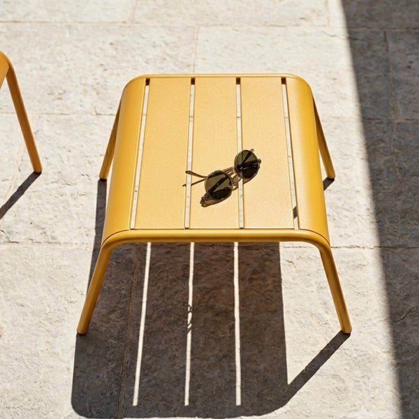 Gelber Beistelltisch aus Metall mit Latten-Design auf einer Steinterrasse.