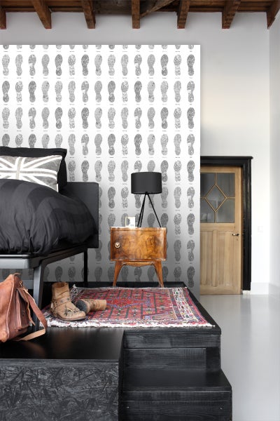 Schlafzimmer mit Bett, Nachttisch, Teppich und Tapete mit Fußabdruckmuster