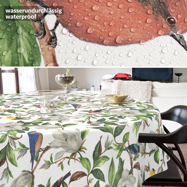 Wasserundurchlässige Tischdecke mit Vogel- und Magnolienmuster auf einem runden Tisch, Nahaufnahme zeigt Wassertropfen auf dem Gewebe.