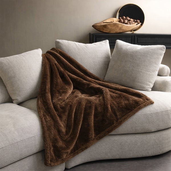 Eine weiche Wohndecke auf einem modernen Sofa mit Kissen in einem wohnlichen Wohnzimmer.