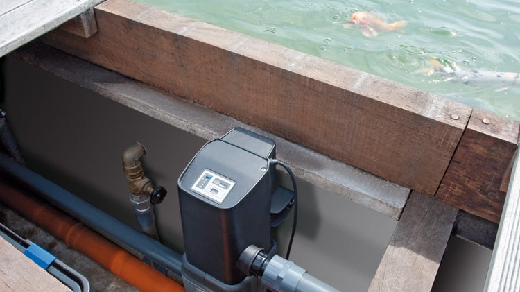 Schwarze Teichpumpensteuerung mit digitalem Display an einem Gartenteich mit Koi-Fischen und Rohrleitungen.