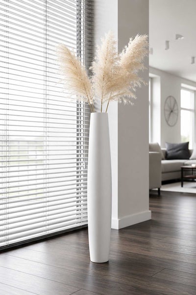 Hohe weiße Bodenvase mit Pampasgras in einem hellen, modernen Wohnzimmer mit dunklem Holzboden und Jalousien.