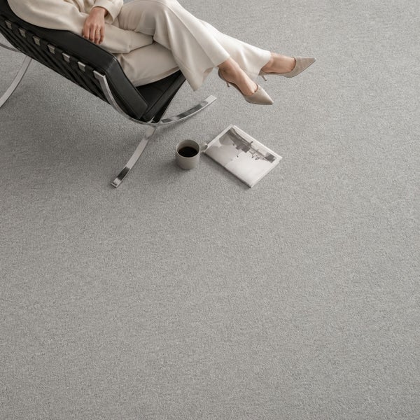 Strukturierter grauer Teppichboden in einem modernen Wohnzimmer mit Designer-Sessel, Kaffeetasse und Zeitschrift auf dem Boden.
