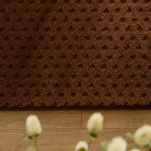 Strukturierter brauner Teppich mit kleinem Rautenmuster auf einem Holzfußboden.