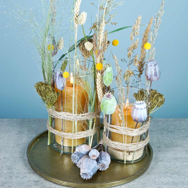 Dekorative Kerzen in Glasvasen mit Trockenblumen auf einem Tablett