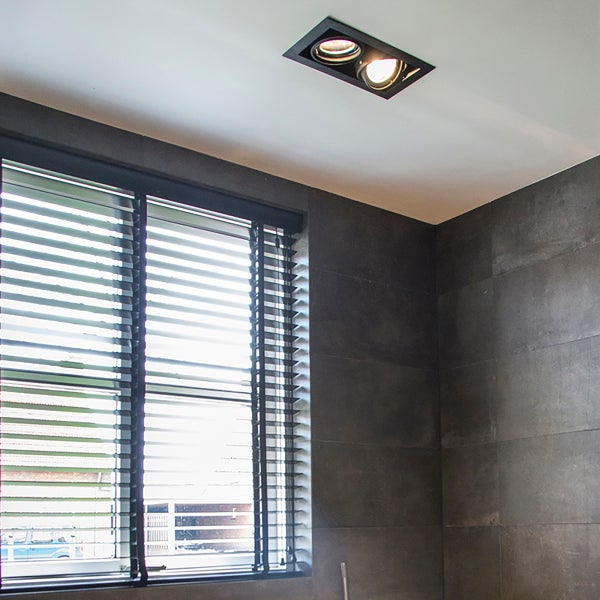 Moderner Innenraum mit einer schwarzen rechteckigen Deckenleuchte mit zwei Spots dunkelgrauen Wandfliesen und Jalousien am Fenster