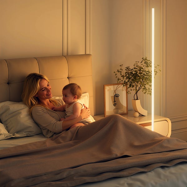 Schlanke LED Stehleuchte als Lichtstab neben einem Bett mit einer Mutter und ihrem Baby in einem modernen Schlafzimmer mit warmer Beleuchtung.