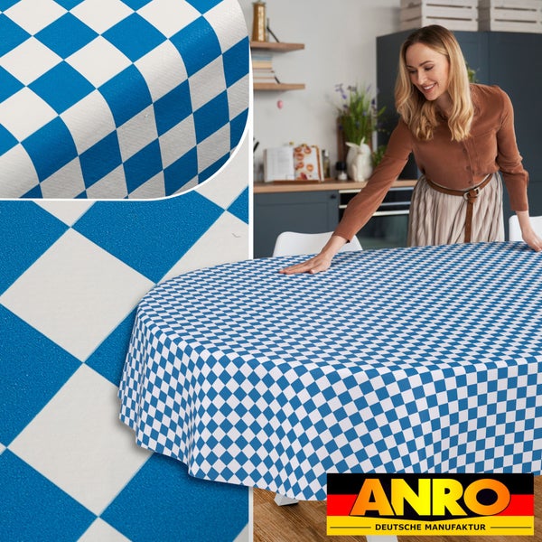 Eine Frau breitet eine blau-weiße Tischdecke mit Rautenmuster auf einem runden Tisch in einer hellen Küche aus. Detailansicht. ANRO Logo.