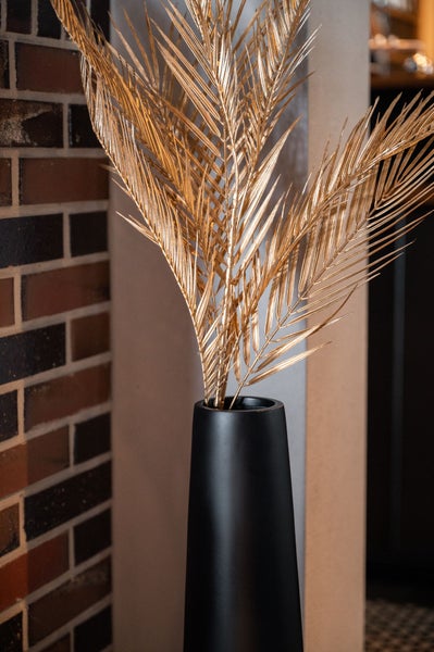 Moderne Inneneinrichtung mit einer hohen schwarzen Bodenvase und goldenen Palmwedeln neben einem gemauerten Kamin vor einer Bar.