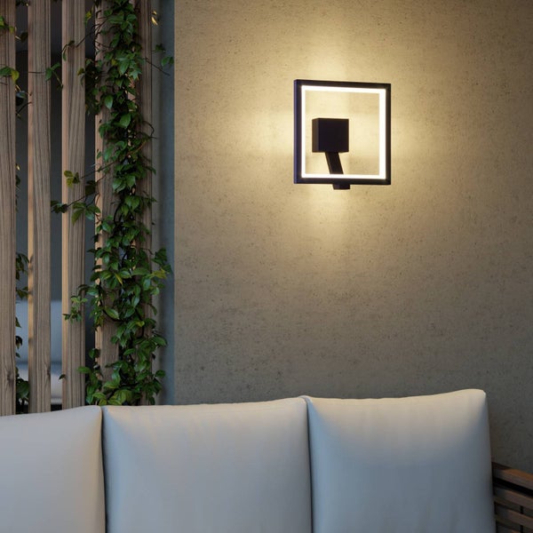 Moderne quadratische LED-Außenwandleuchte an einer strukturierten Wand über einem hellen Sofa im Außenbereich neben einer Pflanze.