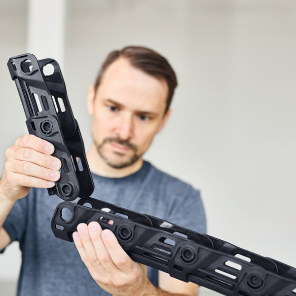 Ein Mann hält zwei schwarze Kunststoffteile für Inline Skates in den Händen und setzt diese zusammen.