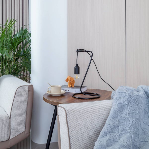 Dekorative Szene mit Tischlampe, Tasse, Dekofigur und Decke auf einem Beistelltisch neben einem Sofa