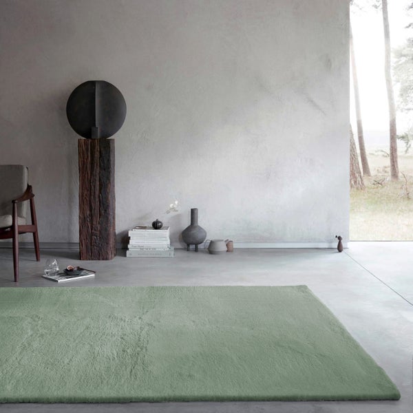 Hochflor-Teppich in einem modern eingerichteten Wohnzimmer mit Betonboden, strukturierter Wand und Holzskulptur.
