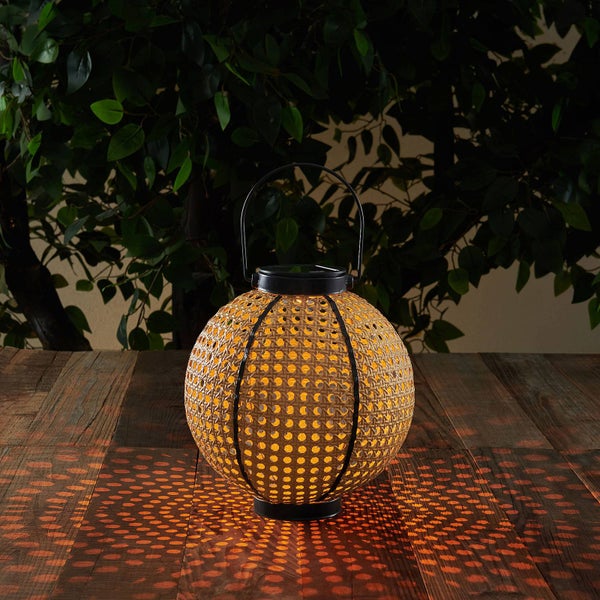 Kugelförmige Solar-Laterne mit dekorativem Rattangeflecht und Metallgriff auf einem Holztisch im Garten.