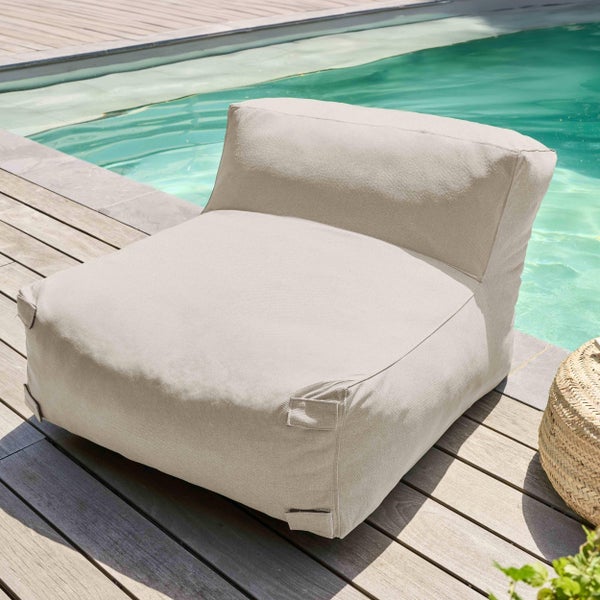 Beigefarbener Outdoor-Sitzsack aus Stoff auf einer hellen Holzterrasse direkt an einem Swimmingpool.