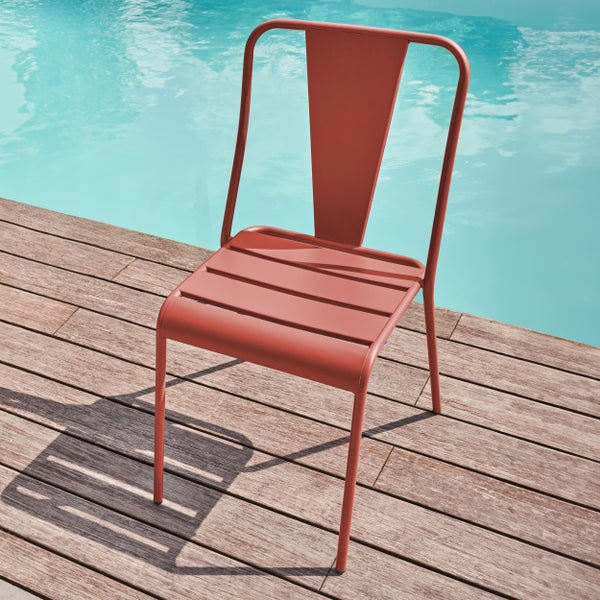 Terracottafarbener Metall-Gartenstuhl auf einer Holzterrasse neben einem Pool. Moderner Stapelstuhl mit Latten-Sitzfläche und Metallgestell.