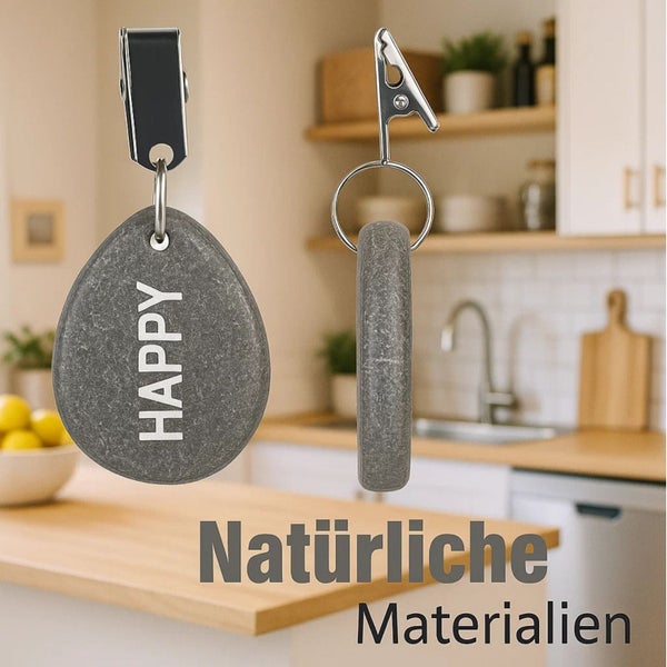 Zwei graue Handtuchhalter aus Stein mit Clip zur Befestigung und Gravur Happy vor einer unscharfen Küchenzeile.