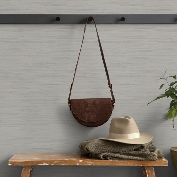 Szene mit brauner Umhängetasche, Hut und Strickjacke auf einer Holzbank vor einer Wand mit Garderobenleiste