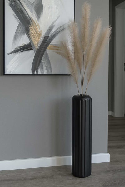 Hohe schwarze Bodenvase mit vertikalen Rillen und getrocknetem Pampasgras in einem modern gestalteten Wohnraum.