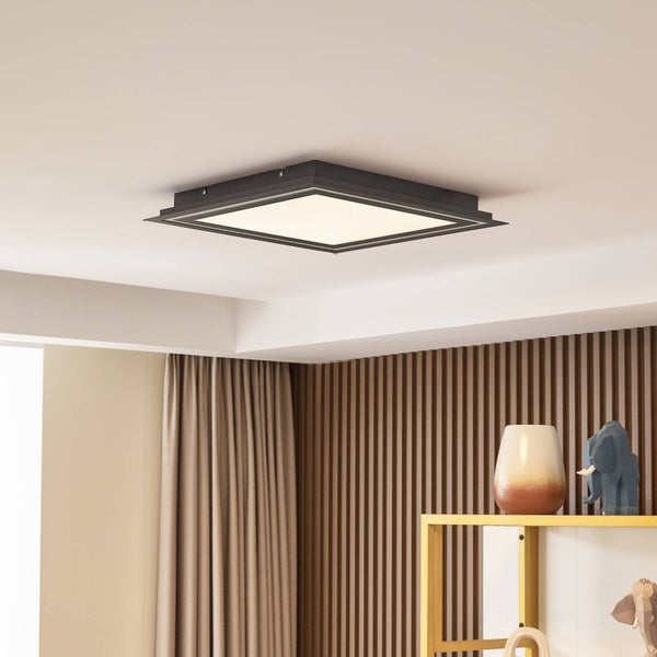 Quadratische Deckenleuchte mit schwarzem Rahmen an der Decke eines hellen, modern eingerichteten Raumes mit einer Wand aus Holzlamellen.