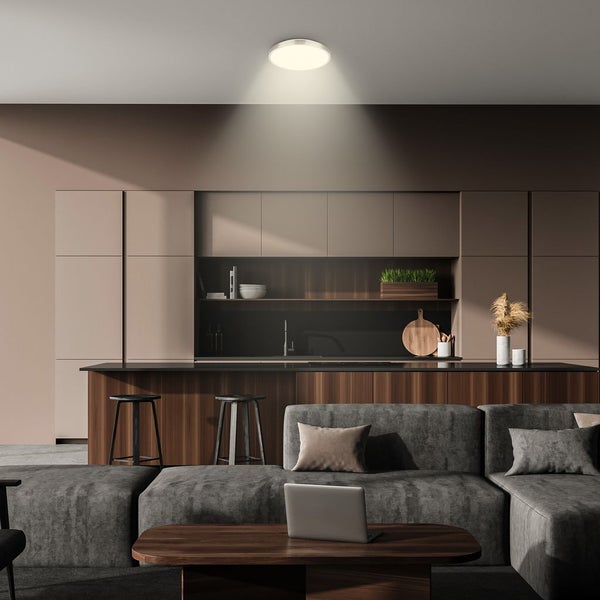 Runde LED-Deckenleuchte in einer modernen Wohnküche, die helles Licht auf ein graues Sofa und eine Kücheninsel wirft.