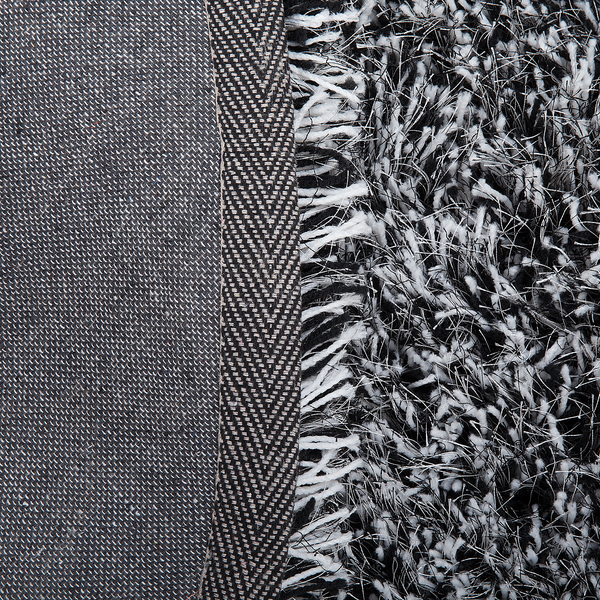 Detailansicht eines Hochflor-Teppichs mit gewebter Rückseite, Kante mit Fischgrätmuster und schwarz-weißem Shaggy-Flor.