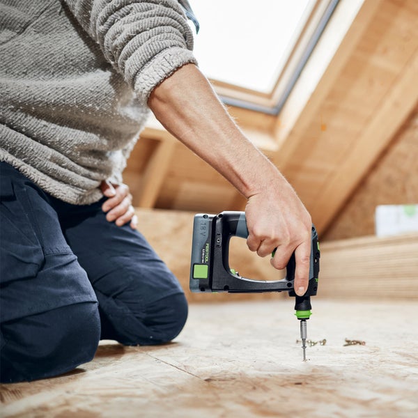 Handwerker befestigt Schraube mit Akku-Bohrschrauber auf Holzdiele in Dachgeschoss