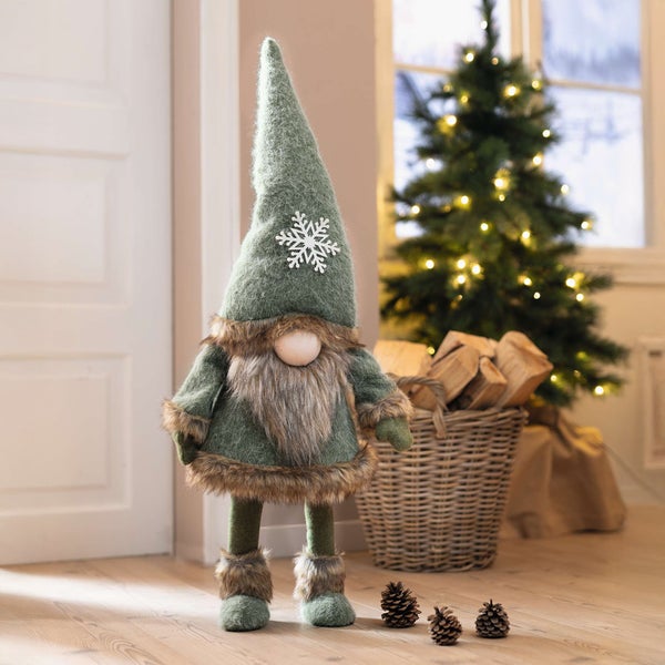 Dekorativer Weihnachtswichtel mit Bart, Schneeflocke auf der Mütze und Weihnachtsbaum im Hintergrund