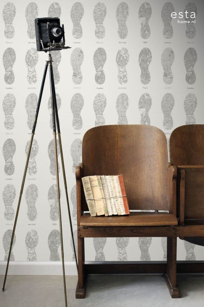 Zimmer mit Fototapete mit Fußabdruck-Muster, Vintage-Kamera auf Stativ und Holzbänken mit Büchern