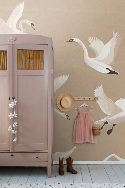 Szene mit einem Kleiderschrank, einer Tapete mit Schwanenmuster, einem Strohhut, einem Kinderkleid und Cowboystiefeln, die ein helles und organisiertes Ambiente schaffen