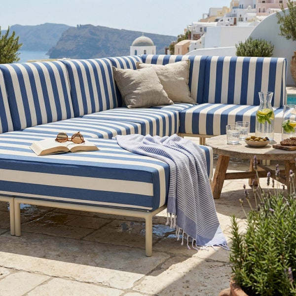 Eckiges Lounge-Sofa mit blau-weiß gestreiften Polstern auf einer hellen Steinterrasse mit Küstenblick und rustikalem Holztisch.